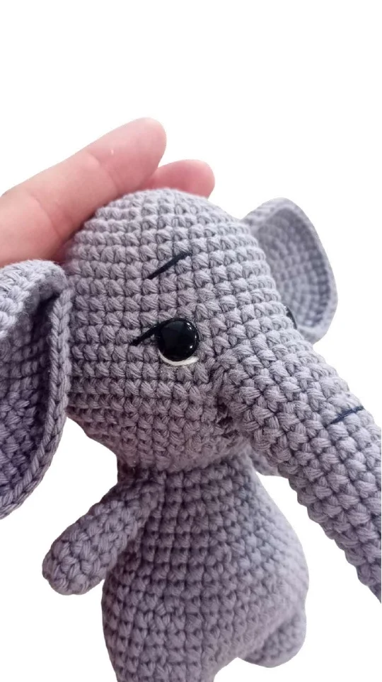 A hand holding a small gray crocheted elephant toy next to a free crochet pumpkin pattern.
