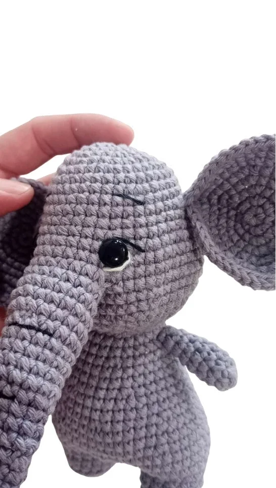 A hand holds a small, grey elephant amigurumi toy.