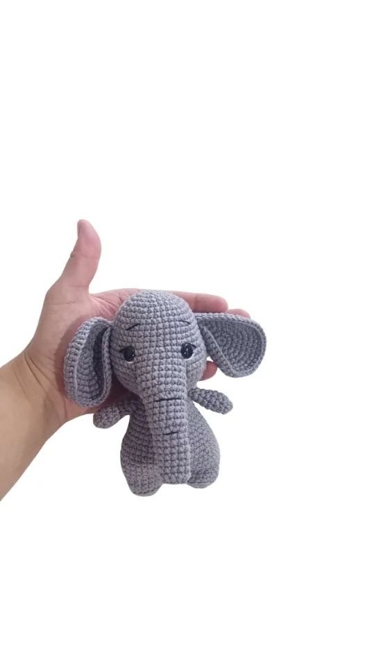 A hand holding a small, gray elephant amigurumi.