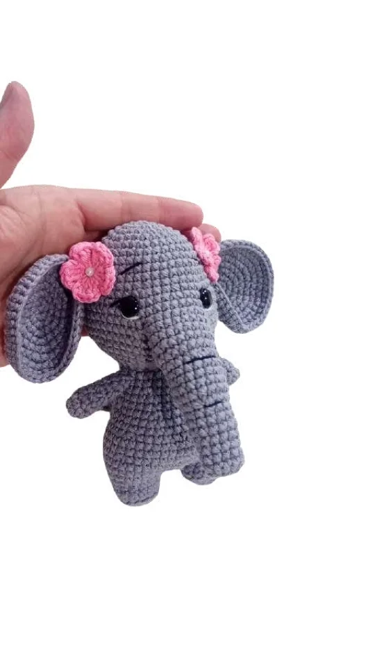 A hand holds a grey elephant amigurumi toy adorned with small pink flowers on its ears.