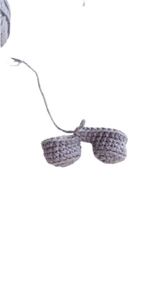 Two small gray crocheted pieces connected by a yarn strand, similar in style to an elephant amigurumi.