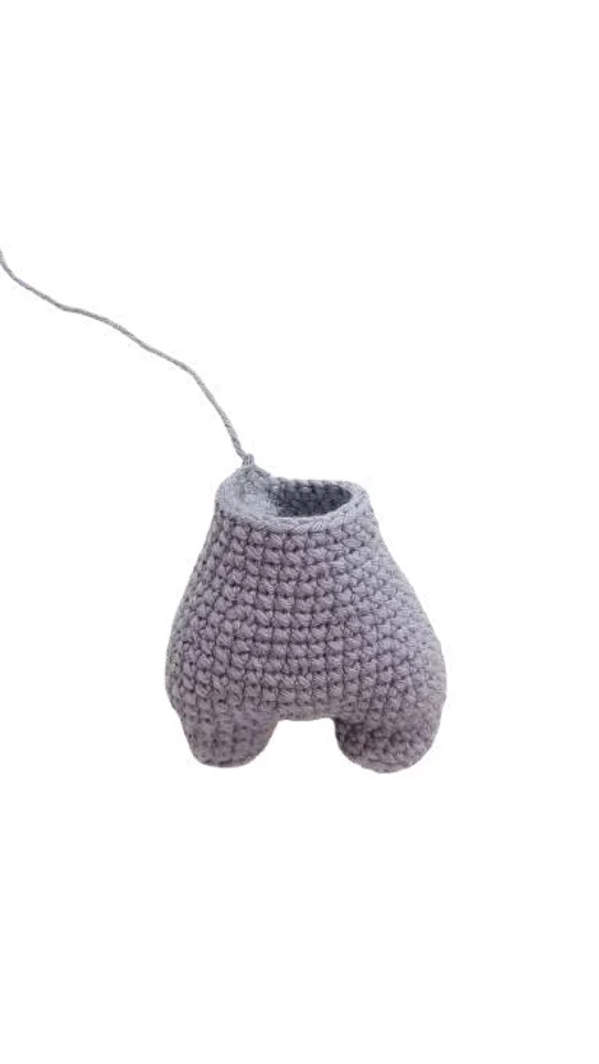 A light purple crocheted figure base with two legs and a trailing piece of yarn, shown as part of a pumpkin crochet pattern.