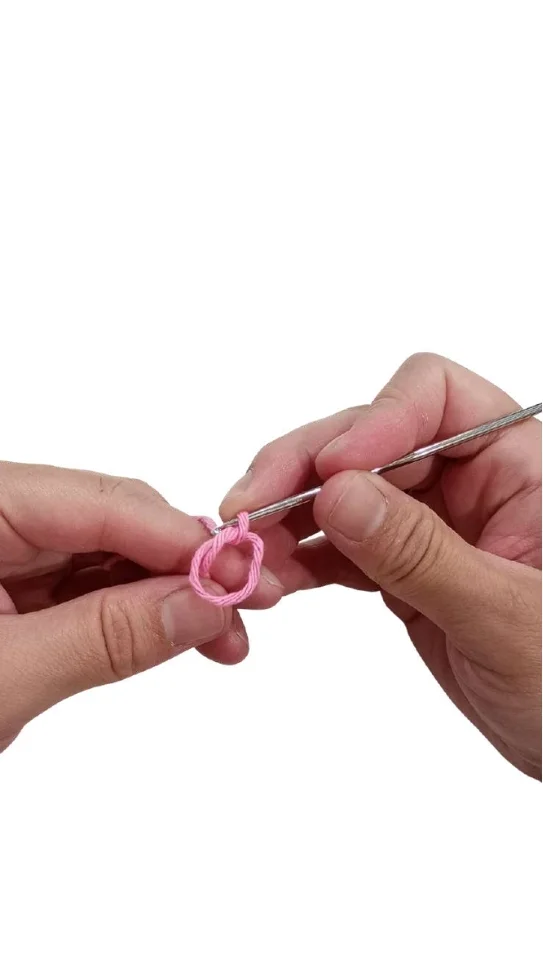Hands holding a crochet hook creating a magic ring with pink yarn, the start of an elephant amigurumi.