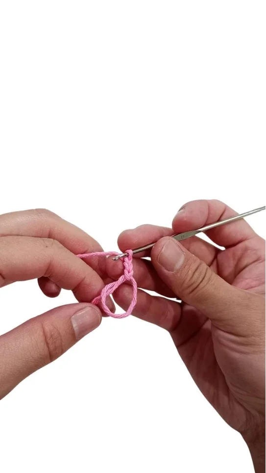 Hands using a crochet hook to work a loop of pink yarn for a crochet pumpkin pattern.