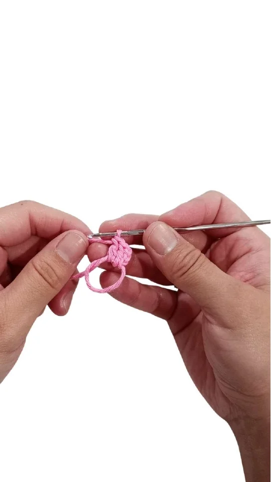Hands crocheting a small pink circle with a metal hook as part of a crochet pumpkin pattern.