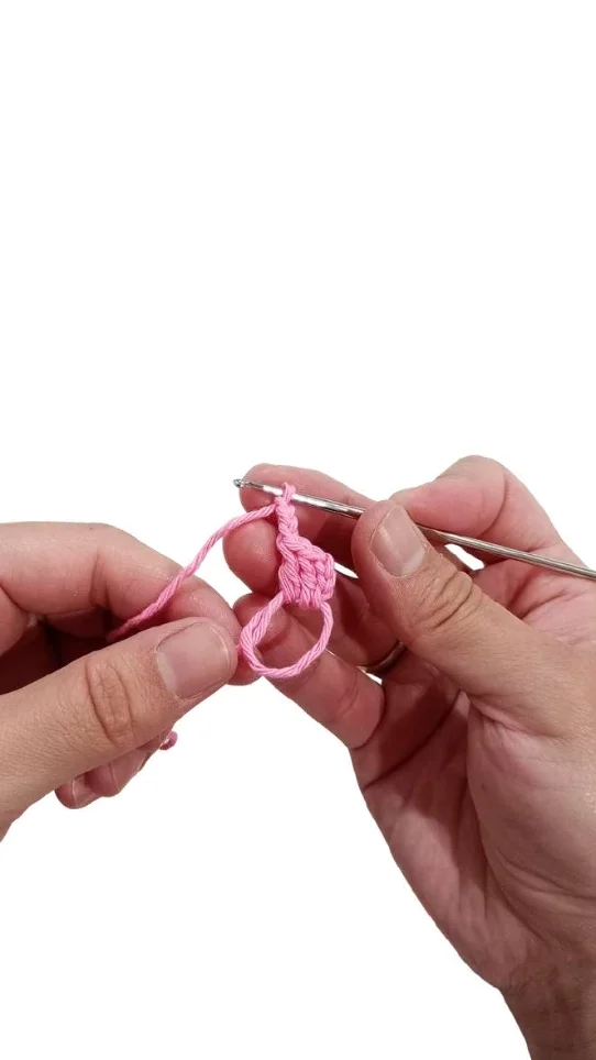 Hands holding a crochet hook and pink yarn, forming stitches into a loop for a crochet pumpkin pattern.