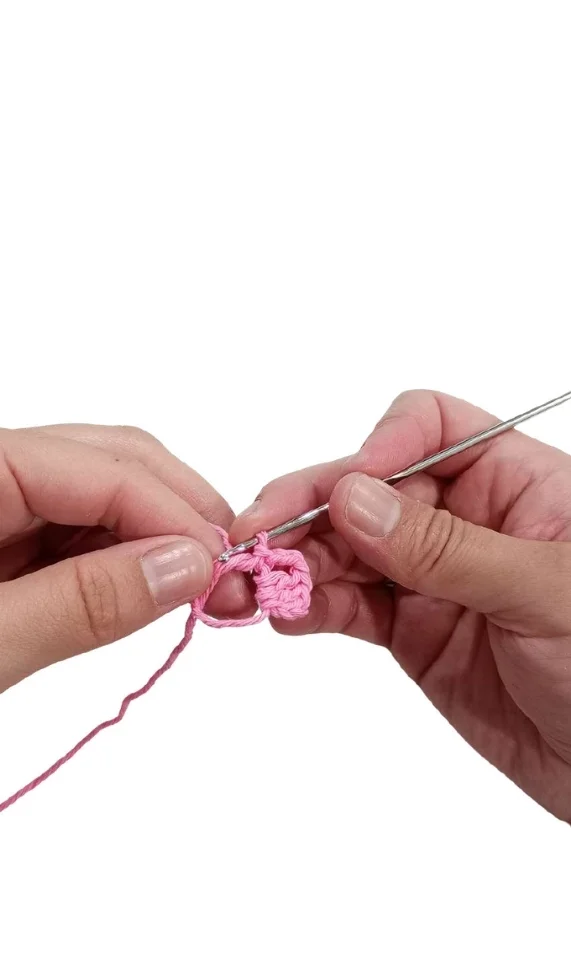 Hands crocheting an elephant amigurumi with pink yarn and a silver hook.