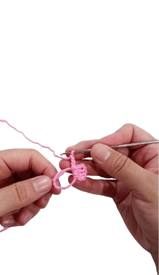 Hands using a crochet hook to work pink yarn into a magic ring for a crochet pumpkin pattern.