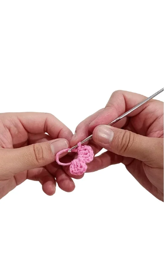 Hands hold a metal crochet hook to work on a small pink yarn motif, inspired by a free crochet pumpkin pattern.