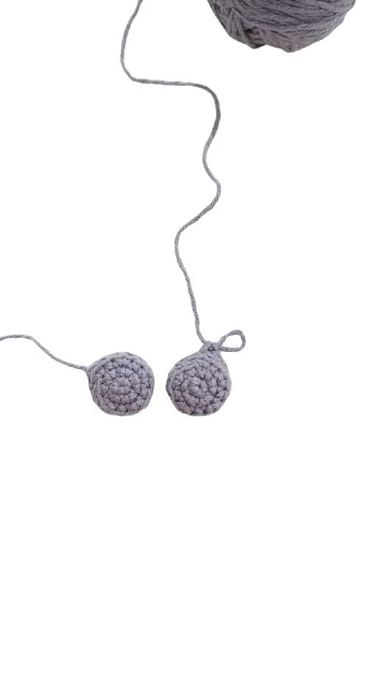 Two small, crocheted gray circles for an elephant amigurumi attached to a ball of yarn by a single strand.