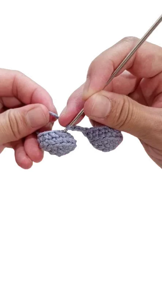 Hands using a metal crochet hook to join two small gray pieces of an elephant amigurumi together.