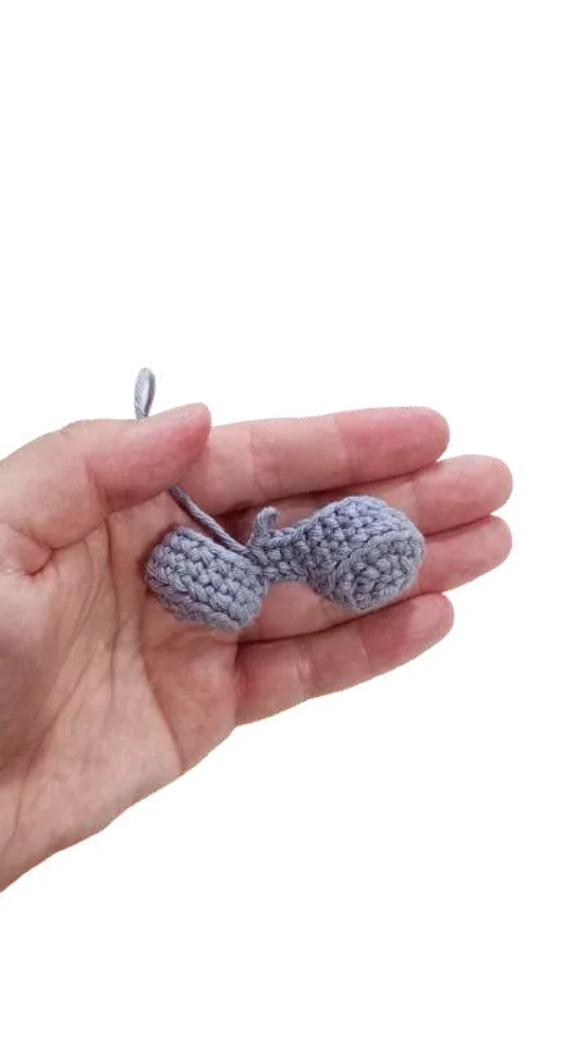 A hand holds a small, gray elephant amigurumi featuring two circular shapes connected by a bridge.