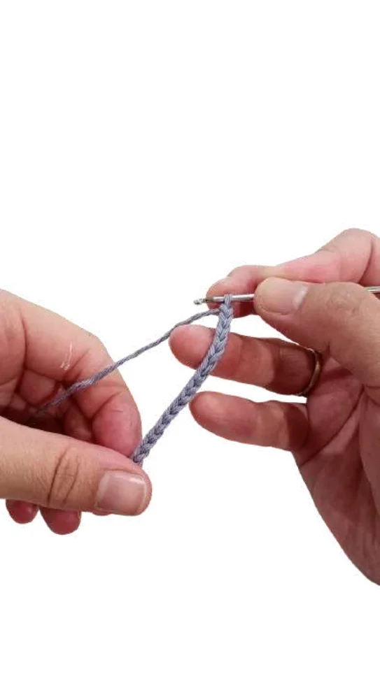 Hands use a metal crochet hook to work a chain of grey yarn for a crochet pumpkin pattern.