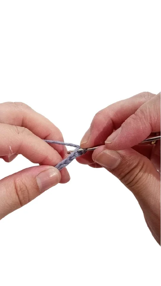 Hands crocheting a chain stitch with blue yarn and a metal hook, a technique used for a free crochet pumpkin pattern.
