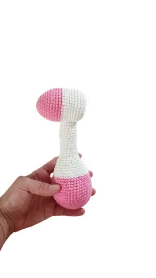 A hand holding a pink and white giraffe amigurumi rattle.
