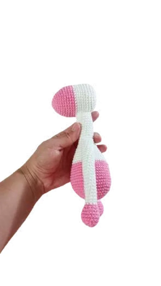 A hand holding a pink and white crocheted baby rattle, similar in style to a giraffe amigurumi.