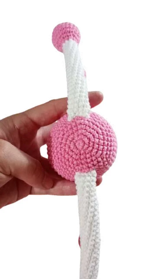 A hand holds a crocheted toy featuring a pink sphere with two long, white, striped extensions, perfect for a free crochet pumpkin pattern.