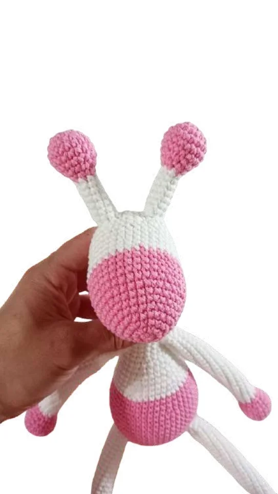 A hand holding a white and pink giraffe amigurumi toy with long antennae.
