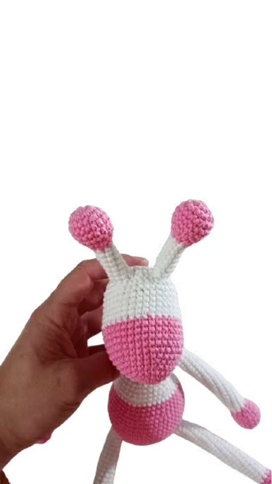 A hand holding a white and pink giraffe amigurumi toy with antennae.
