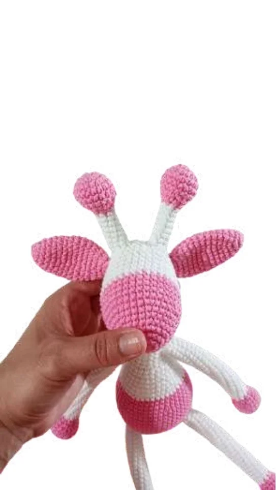 A hand holds a pink and white giraffe amigurumi toy.