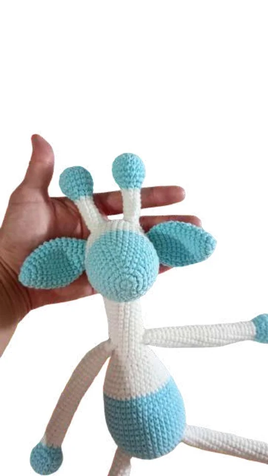 A hand holds a white and light blue giraffe amigurumi toy.