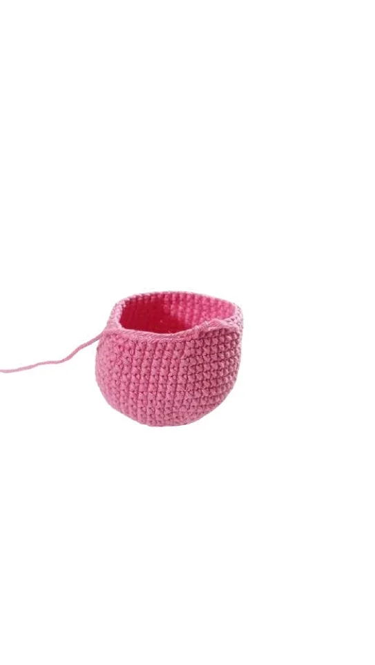 Small, round, pink crocheted bowl featuring a crochet pumpkin pattern design with a loose strand of yarn attached.