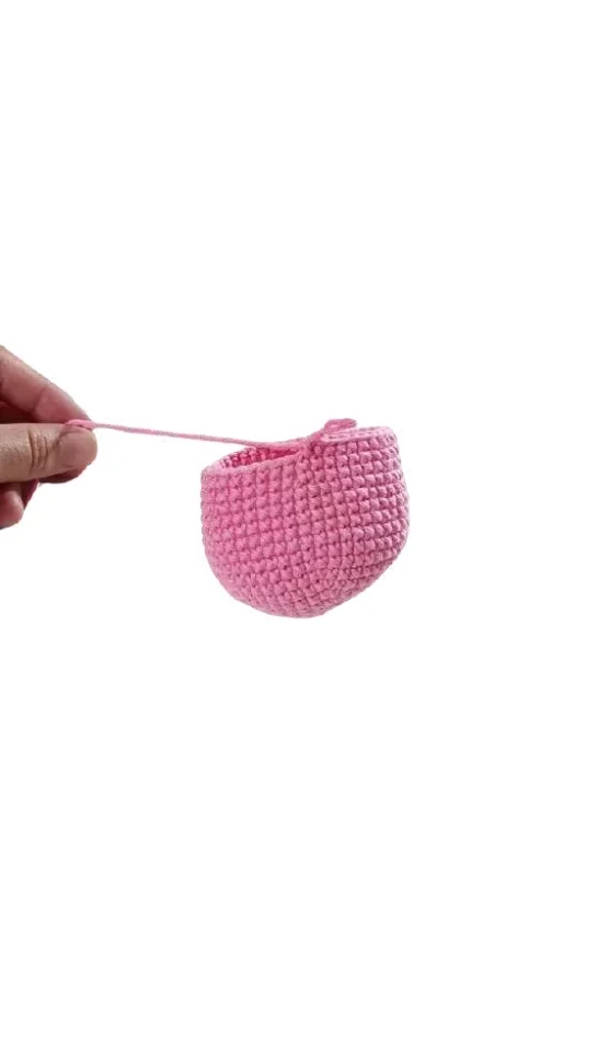 A hand holds a small, bowl-shaped piece of pink crochet from a free crochet pumpkin pattern.