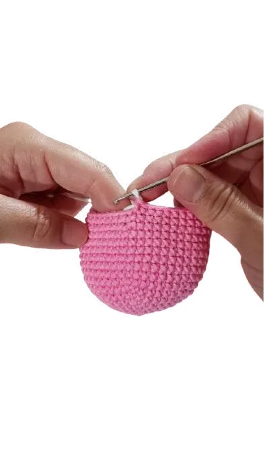 Hands using a metal crochet hook to work on a pink piece for a free crochet pumpkin pattern.