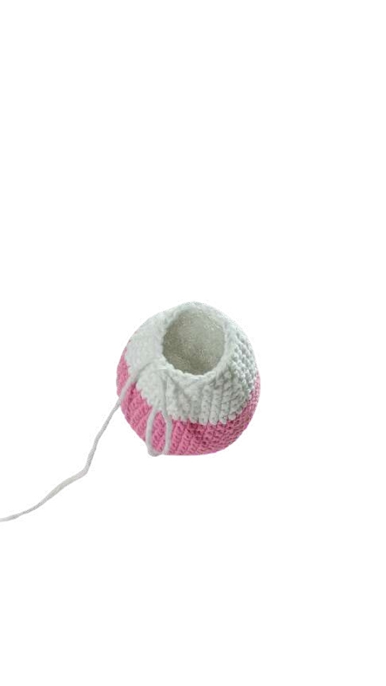 A partially crocheted pumpkin pattern ball in white and pink yarn with a dangling thread.