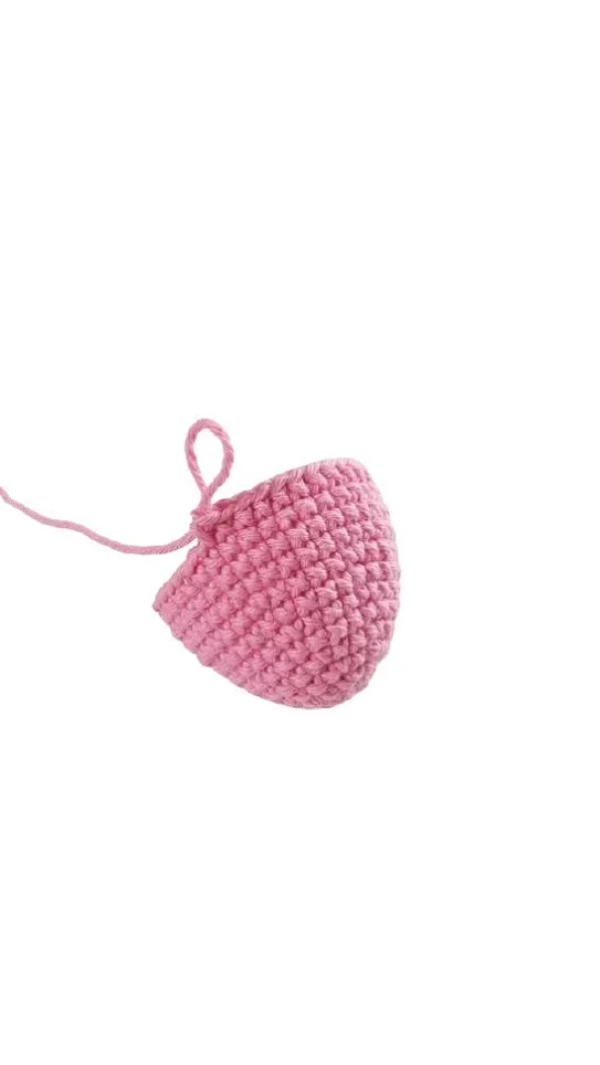 A small, pink, cone-shaped piece of crochet work with a loose yarn tail, similar to the start of a free crochet pumpkin pattern.
