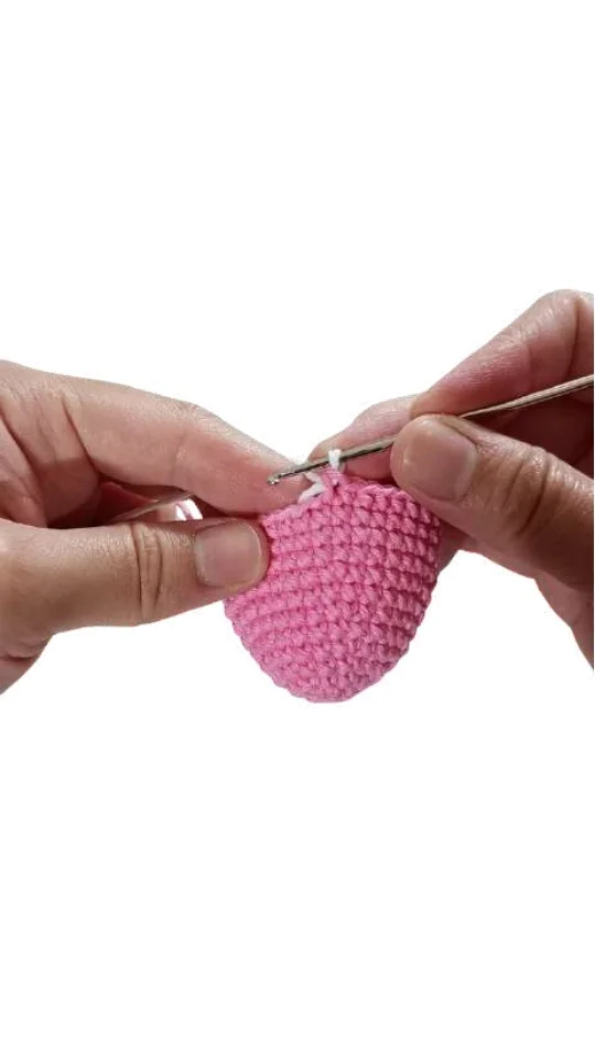 Hands using a silver crochet hook to work a stitch into a pink crocheted piece from a free crochet pumpkin pattern.