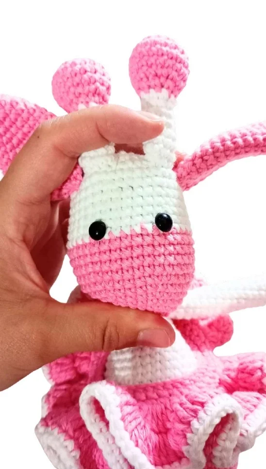 A hand holds a handmade pink and white giraffe amigurumi toy.