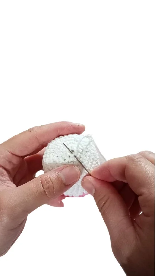 Hands sewing a white crocheted piece with a needle and thread to follow a crochet pumpkin pattern.