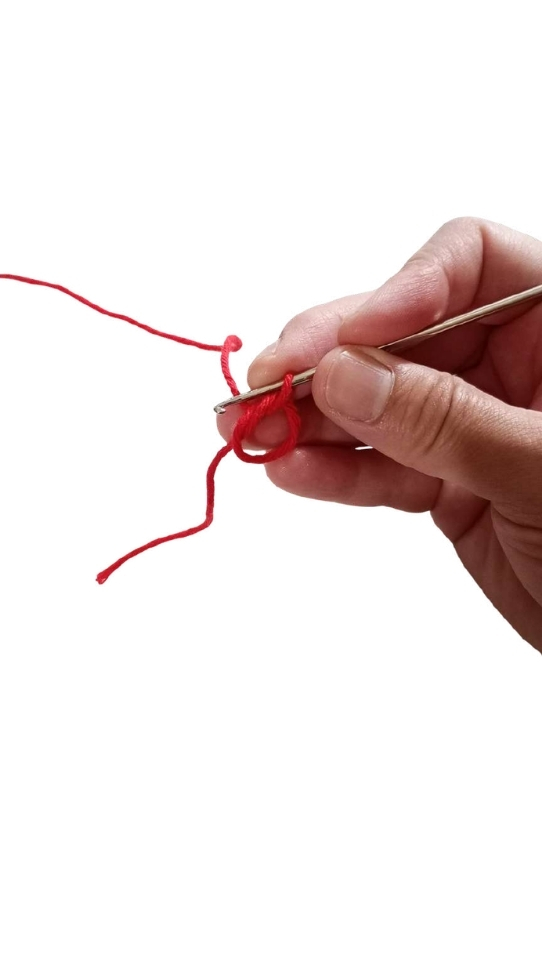 Hand holding a crochet hook to begin a magic ring with red yarn for a crochet pumpkin pattern.