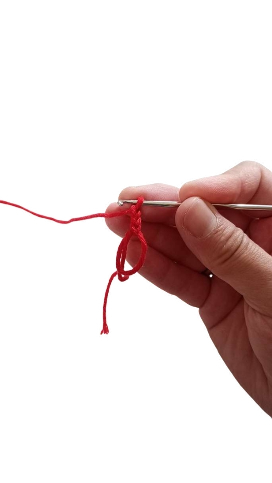A hand holds a crochet hook and red yarn to form a loop for a pumpkin crochet pattern.
