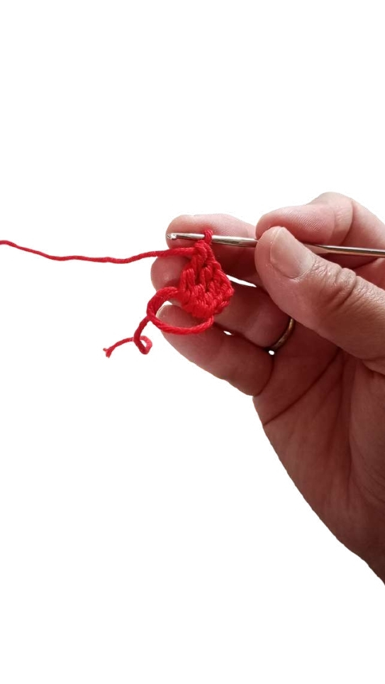 A hand holding a silver crochet hook working with bright red yarn to create a pumpkin crochet pattern.