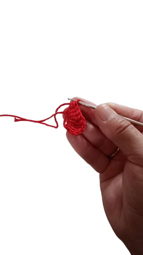 A hand holds a crochet hook while working with red yarn to follow a pumpkin crochet pattern.