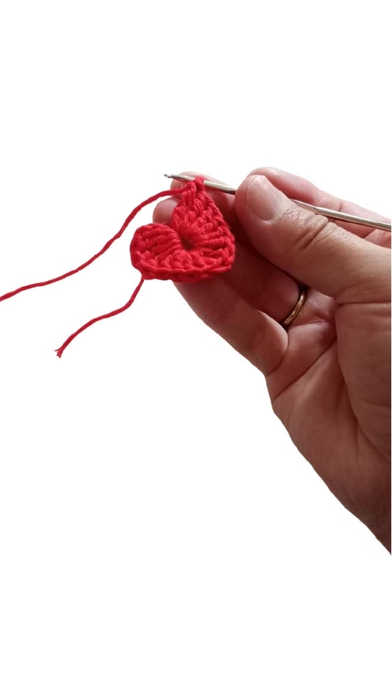 A hand holds a crochet hook, working on a small red heart that could be a fun variation of a free crochet pumpkin pattern.