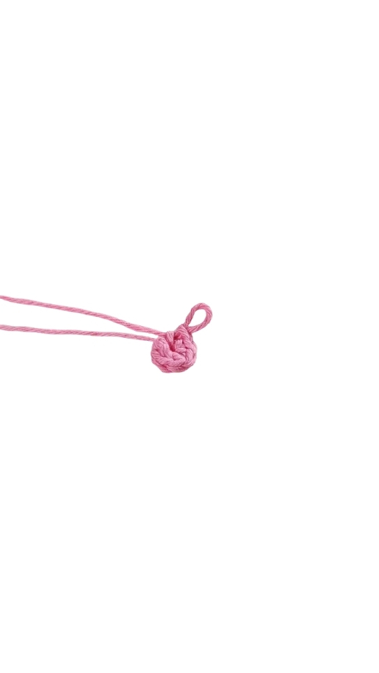 A small, pink crocheted ring with a loop of yarn, styled like a crochet pumpkin pattern.