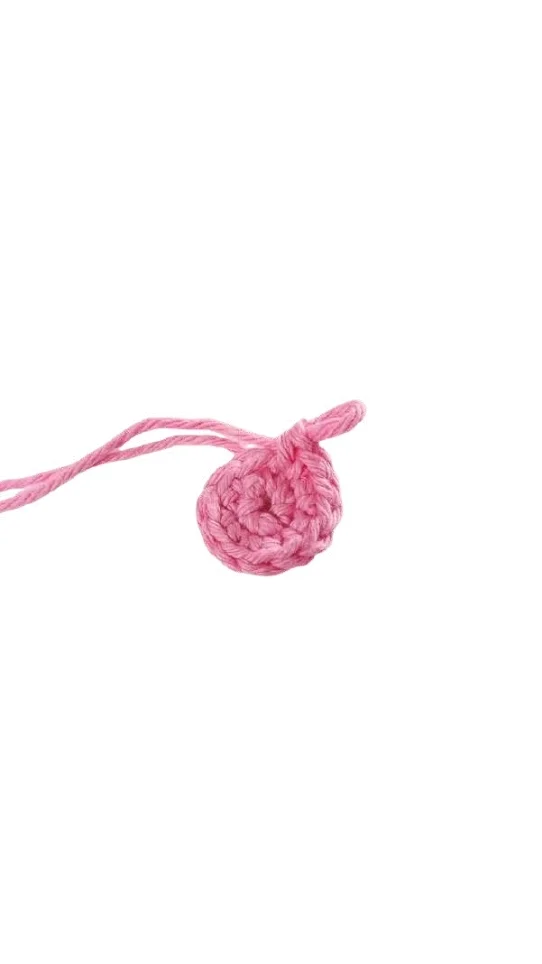 A small pink crocheted circle with an attached yarn tail, perfect for a pumpkin crochet pattern.