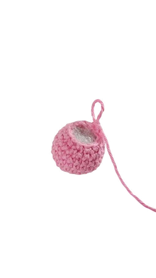 A small, partially crocheted pink pumpkin pattern sphere with a loop of yarn at the top.