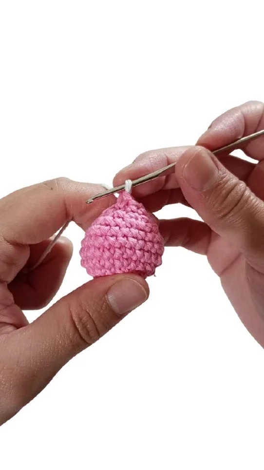 Hands use a crochet hook to work white yarn into a pink, sphere-shaped piece from a crochet pumpkin pattern.