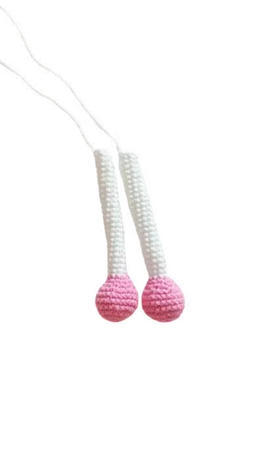 Two crocheted white tubes ending in pink spheres, connected by white strings in this free crochet pumpkin pattern.