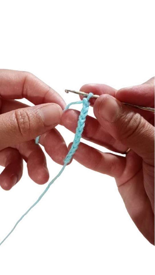 Hands hold a crochet hook and a light blue yarn chain for a free crochet pumpkin pattern.