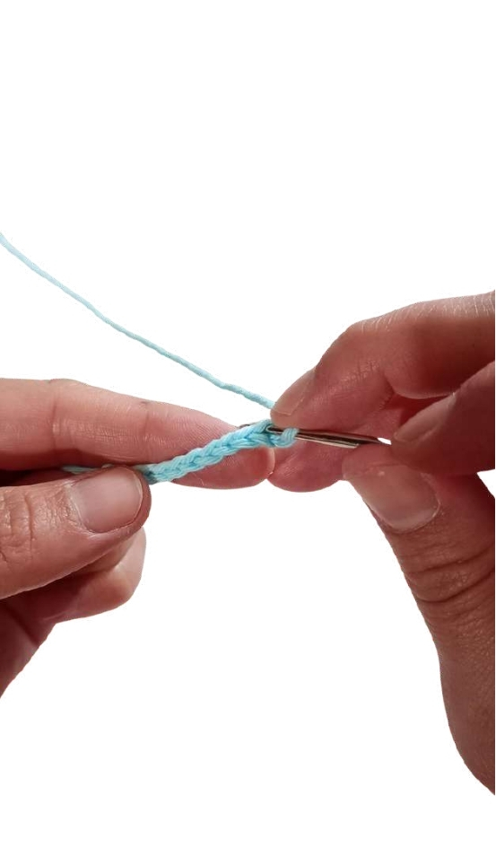 Hands crocheting a chain with light blue yarn for a crochet pumpkin pattern.