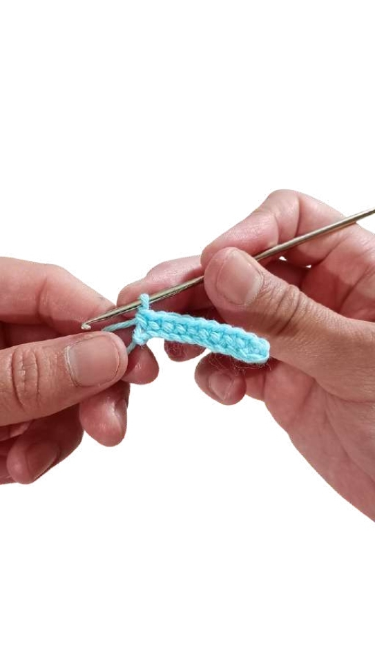Hands holding a metal crochet hook while working a row of light blue yarn stitches for a giraffe amigurumi.