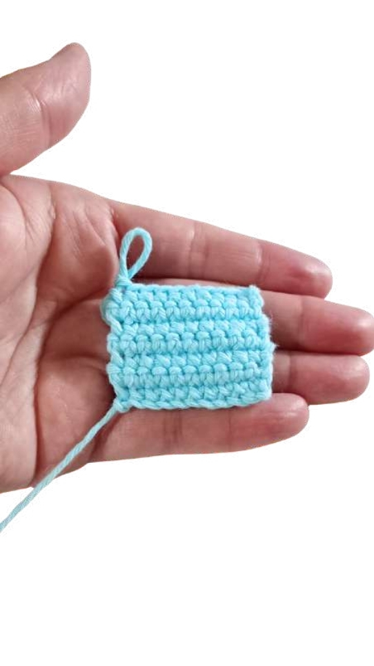 A small, square swatch of light blue crochet held in a person’s palm, reminiscent of the textures seen in a pumpkin crochet pattern.