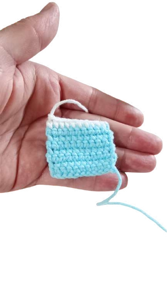 A hand holds a small, square piece of light blue and white crochet work, perfect for a free crochet pumpkin pattern.
