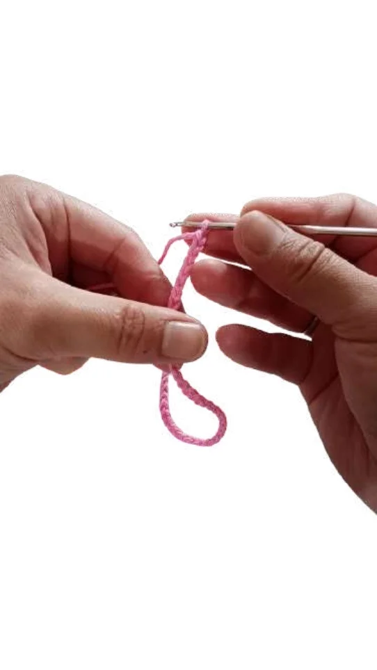 Hands holding a crochet hook and a pink yarn foundation chain for a giraffe amigurumi.