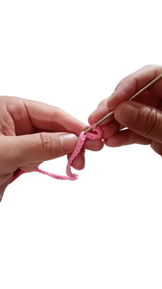 Hands using a metal crochet hook to work a chain stitch with pink yarn for a crochet pumpkin pattern.